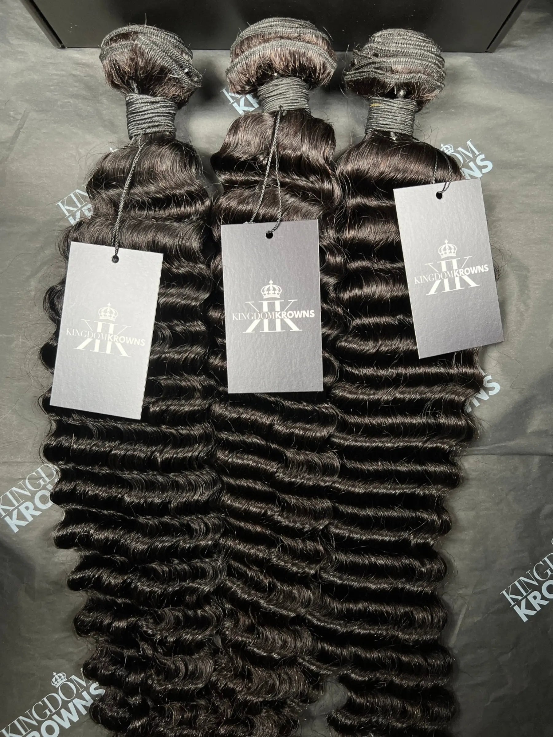 Three bundles of hair extensions with King domKrown labels on a gray surface.