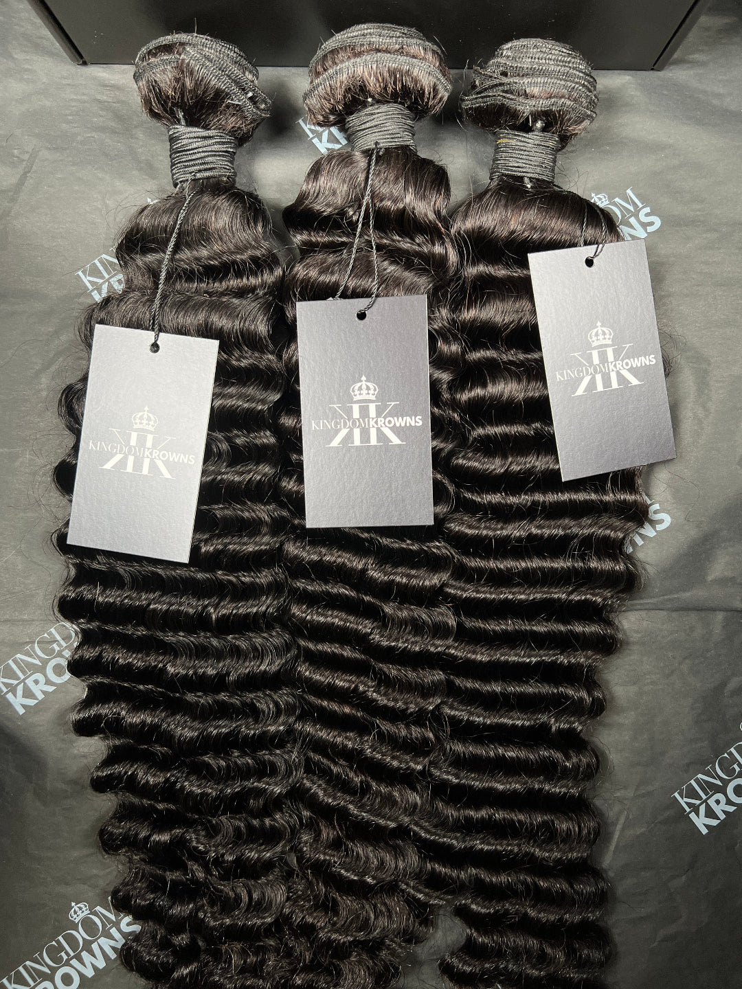 Three bundles of hair extensions with King domKrown labels on a gray surface.