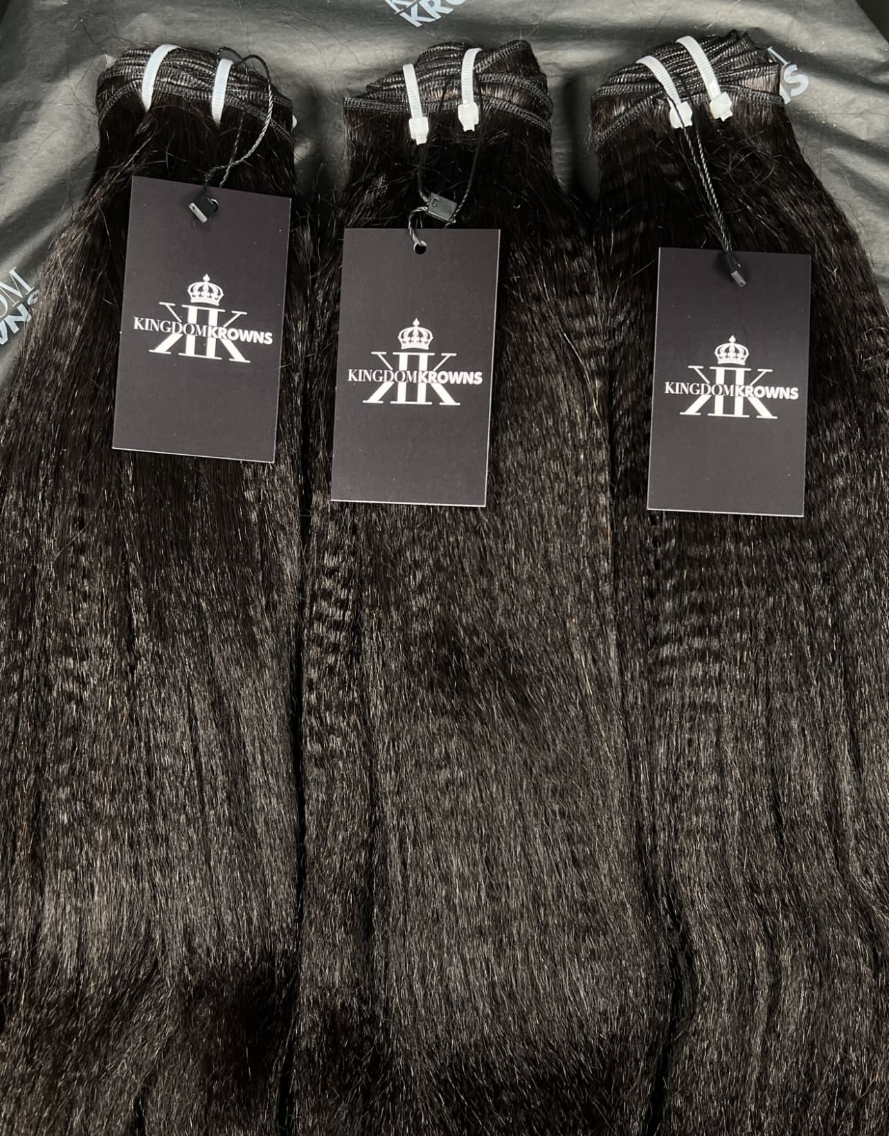Three bundles of hair extensions with Kingdom Krowns brand tags on a textured surface.