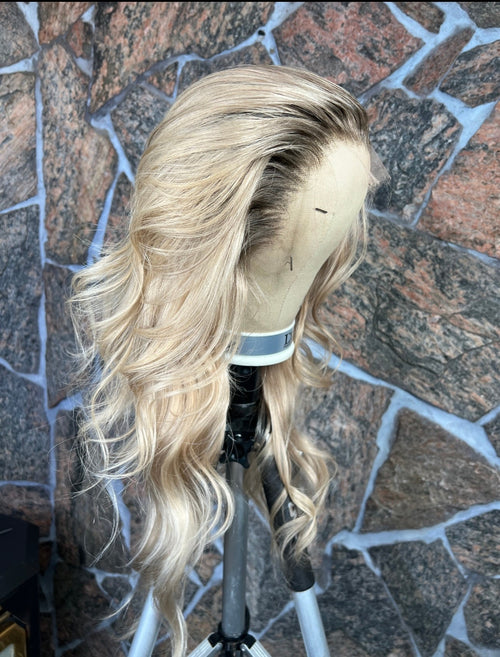 Blonde human hair wig on a mannequin head against a stone wall background