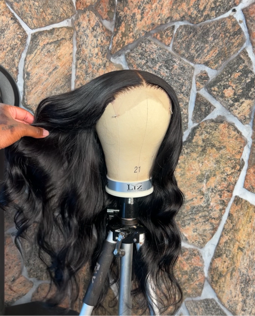 Black human hair wig on a mannequin head against a stone wall background