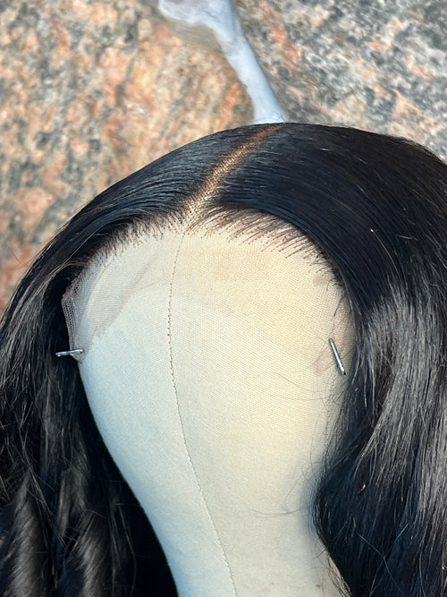 Close-up of a human hair wig with a visible pin on a textured surface