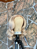 Blonde human hair wig on a mannequin head against a stone wall background
