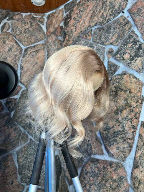 Blonde human hair wig on a stand against a stone pavement background
