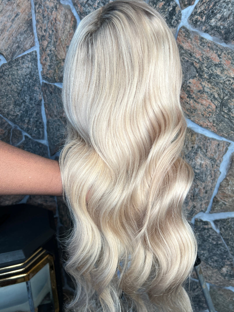 Blonde human hair wig on a mannequin head against a stone wall background